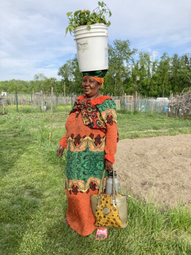 African Woman In Orange Walking With Pail On Head